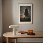 Framed 'Arrival' teletubby movie poster on a wall above a table with a lamp, book, and candle.