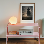 Pink side table with a lamp, books, and a framed movie poster on a wall.