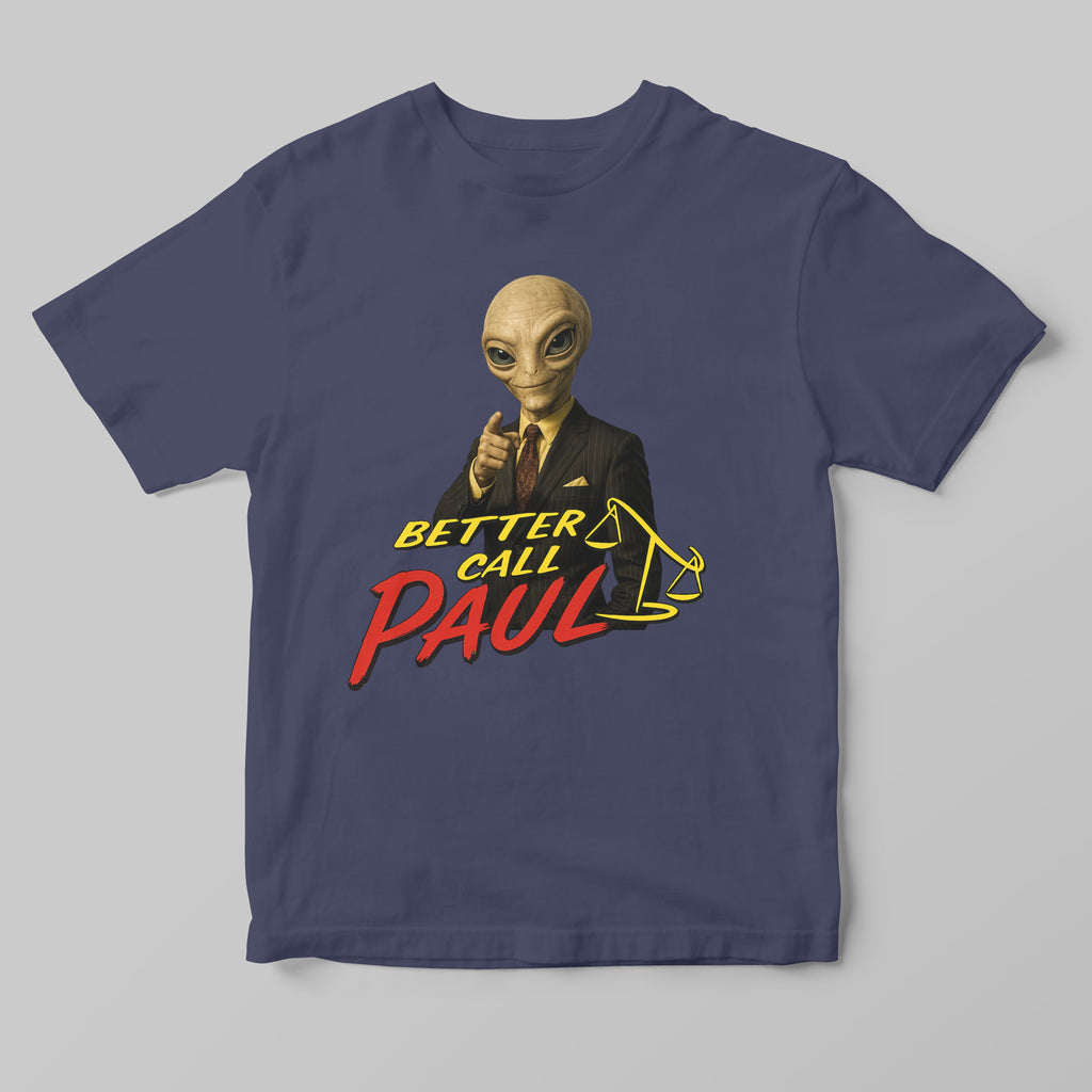 A navy blue short-sleeve t-shirt with a graphic print of a bald alien in a black suit pointing forward, above the text 'BETTER CALL PAUL' in yellow and red, and a yellow gavel illustration, shown on a neutral gray background.
