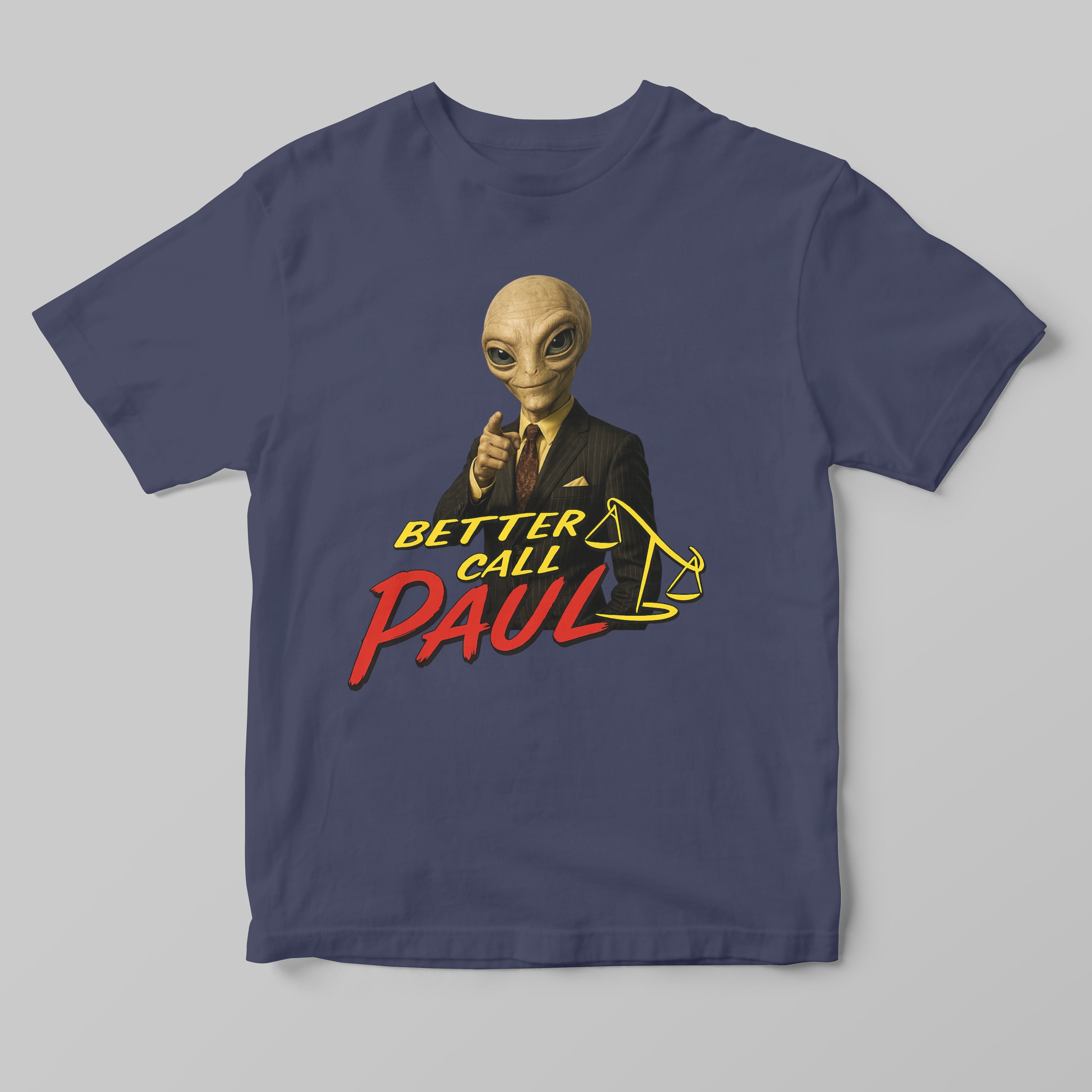 A navy blue short-sleeve t-shirt with a graphic print of a bald alien in a black suit pointing forward, above the text 'BETTER CALL PAUL' in yellow and red, and a yellow gavel illustration, shown on a neutral gray background.