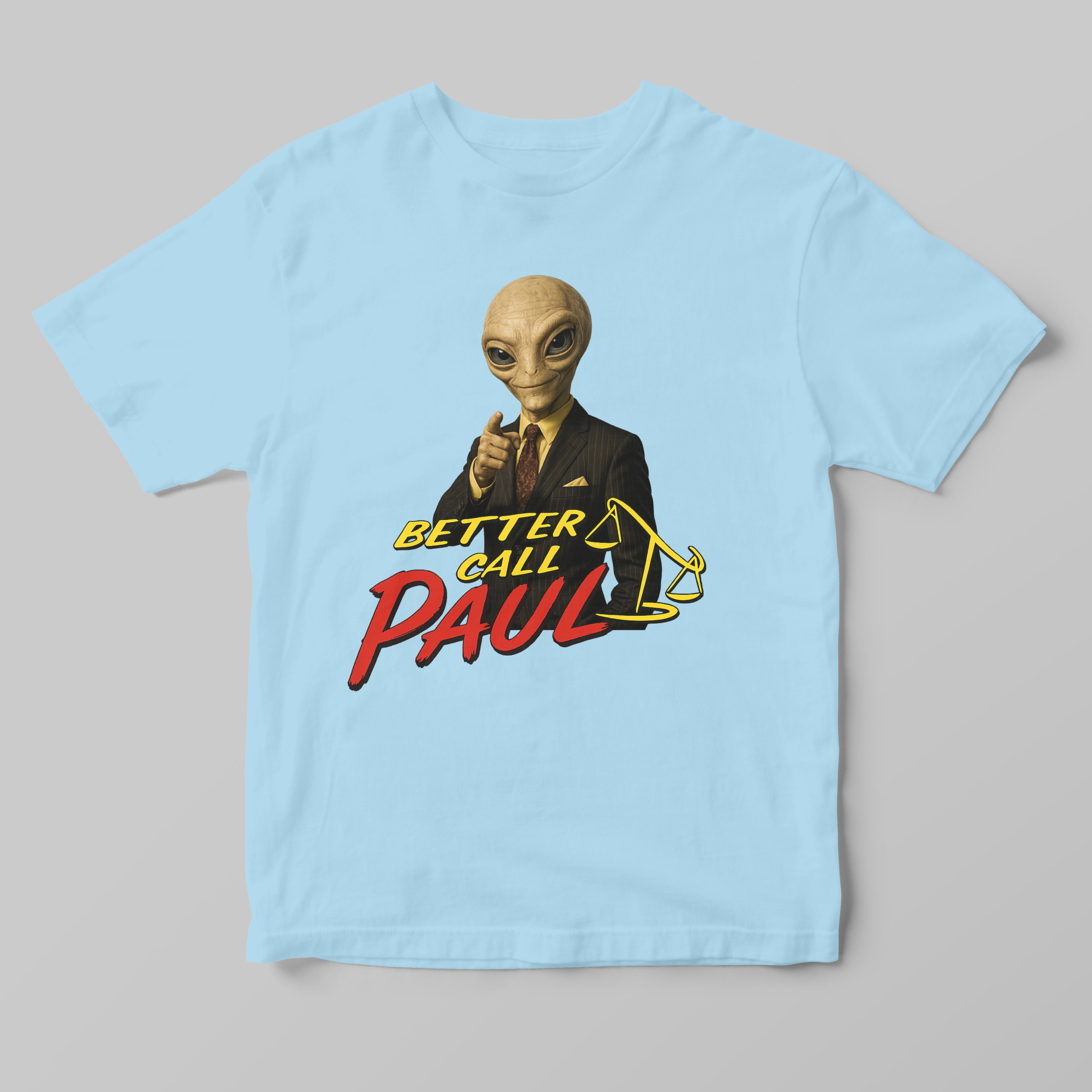 A light blue short-sleeve t-shirt with a graphic print of an alien in a suit pointing forward, with the text 'BETTER CALL PAUL' in yellow and red, on a solid gray background.