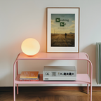 Pink shelf with a lamp, books, and a Breaking Bad sad poster on a white wall.