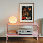 Pink shelf with a lamp, books, and an amplifier against a wall with a framed Die Hard movie poster.