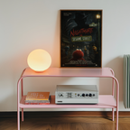 Pink shelf with a lamp, books, and a vintage radio player against a wall with a 'Nightmare on Sesame Street' poster.