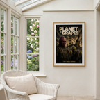 Framed 'Planet of the Grapes' poster on a wall with a window showing flowers.