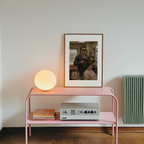 Pink shelf with a lamp, records, and framed picture on a white wall.