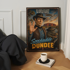 Framed poster of an australian spock character with spockadile dundee text and landscape, placed on a wooden surface with a cup and book.