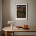 Framed 'Squid Game' poster on a wall above a table with a lamp, book, and candle.