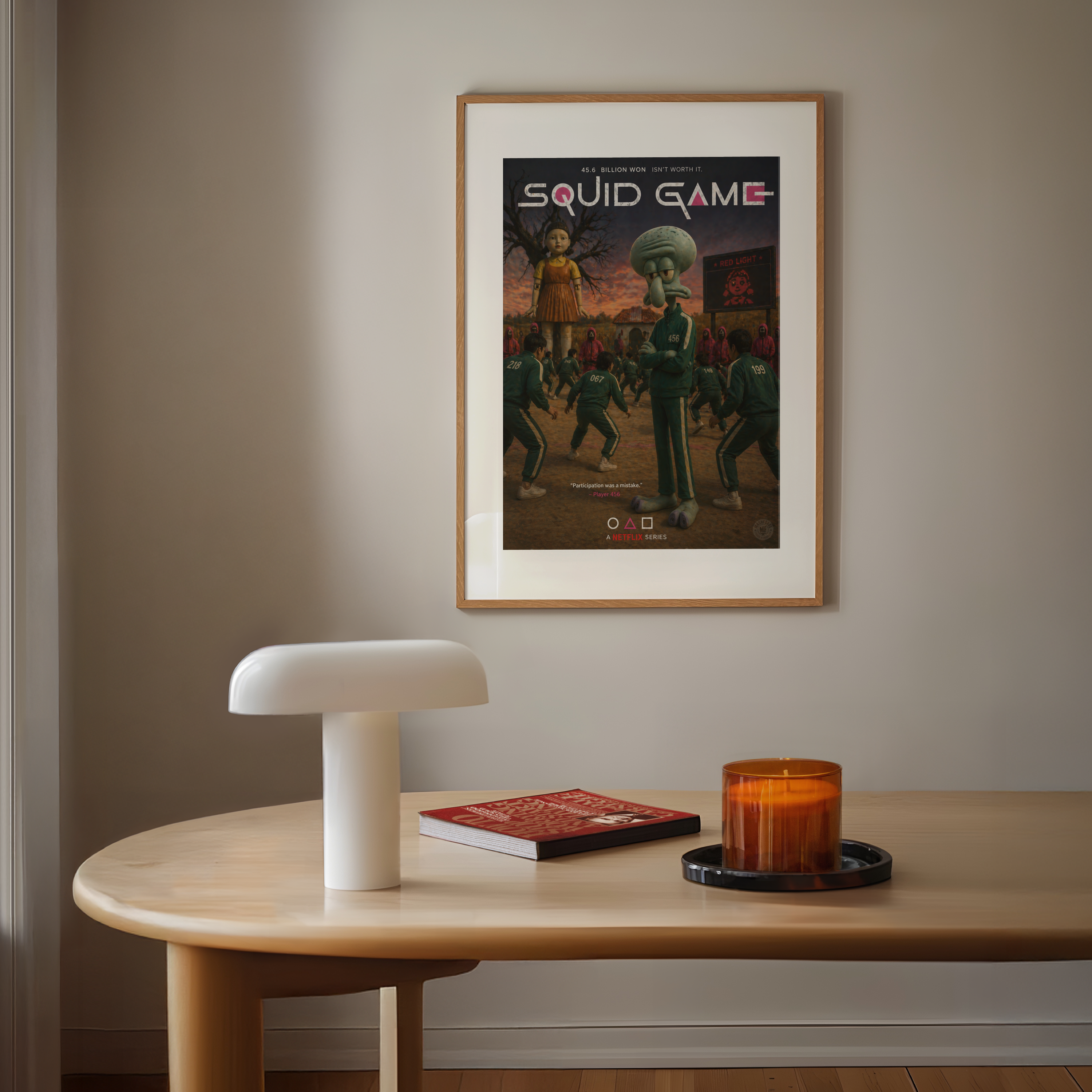 Framed 'Squid Game' poster on a wall above a table with a lamp, book, and candle.