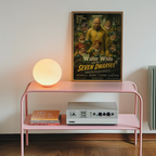Pink shelf with a lamp, books, and a vintage-style poster of 'Walter White and the Seven Dwarves' on a white wall.
