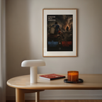 Framed waterboy vs hellboy movie poster on a wall above a wooden table with a lamp, book, and candle.