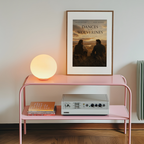 Pink shelf with a lamp, records, and a framed poster on a white wall.