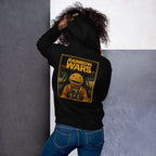 Person wearing a black hoodie with rainbow wars text on the back, standing against a gray wall.