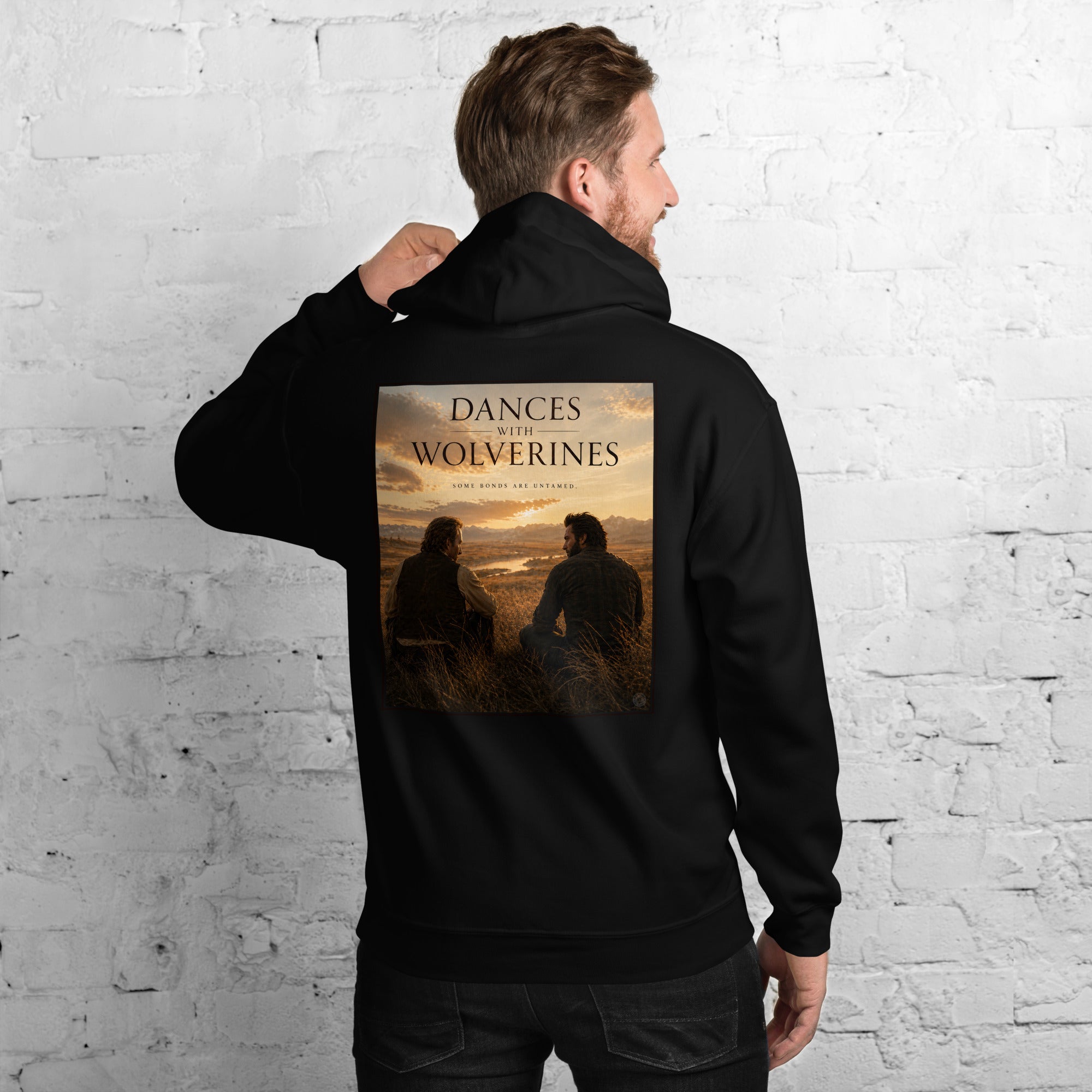 Person wearing a black hoodie with 'Dances with Wolverines' graphic on the back against a white brick wall.