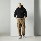 Person wearing a mashforge black hoodie, beige cap, and brown cargo pants against a white background