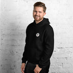 Man wearing a black hoodie with a logo on a white brick wall