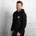 Man wearing a black hoodie with a mashforge logo on a white brick wall
