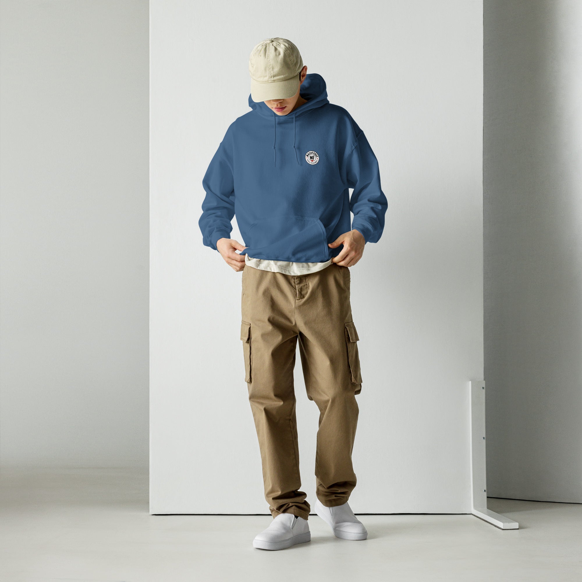 Person wearing a blue hoodie and brown cargo pants standing against a white wall.