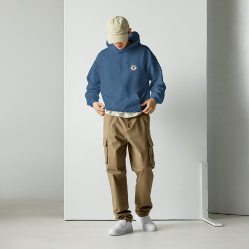 Person wearing a blue hoodie and brown cargo pants standing against a white wall.
