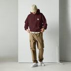 Person wearing a maroon hoodie with mashforge logo, beige cap, and brown cargo pants against a white background