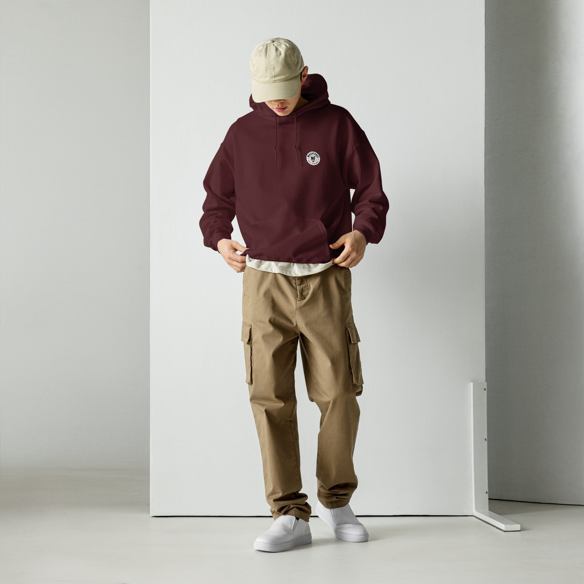 Person wearing a maroon hoodie with mashforge logo, beige cap, and brown cargo pants against a white background
