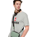 A man wearing a light gray crewneck t-shirt with a black and red 'PiBWASSER' logo on the chest, styled with a patterned neck scarf and a sage green crossbody bag with a black strap.