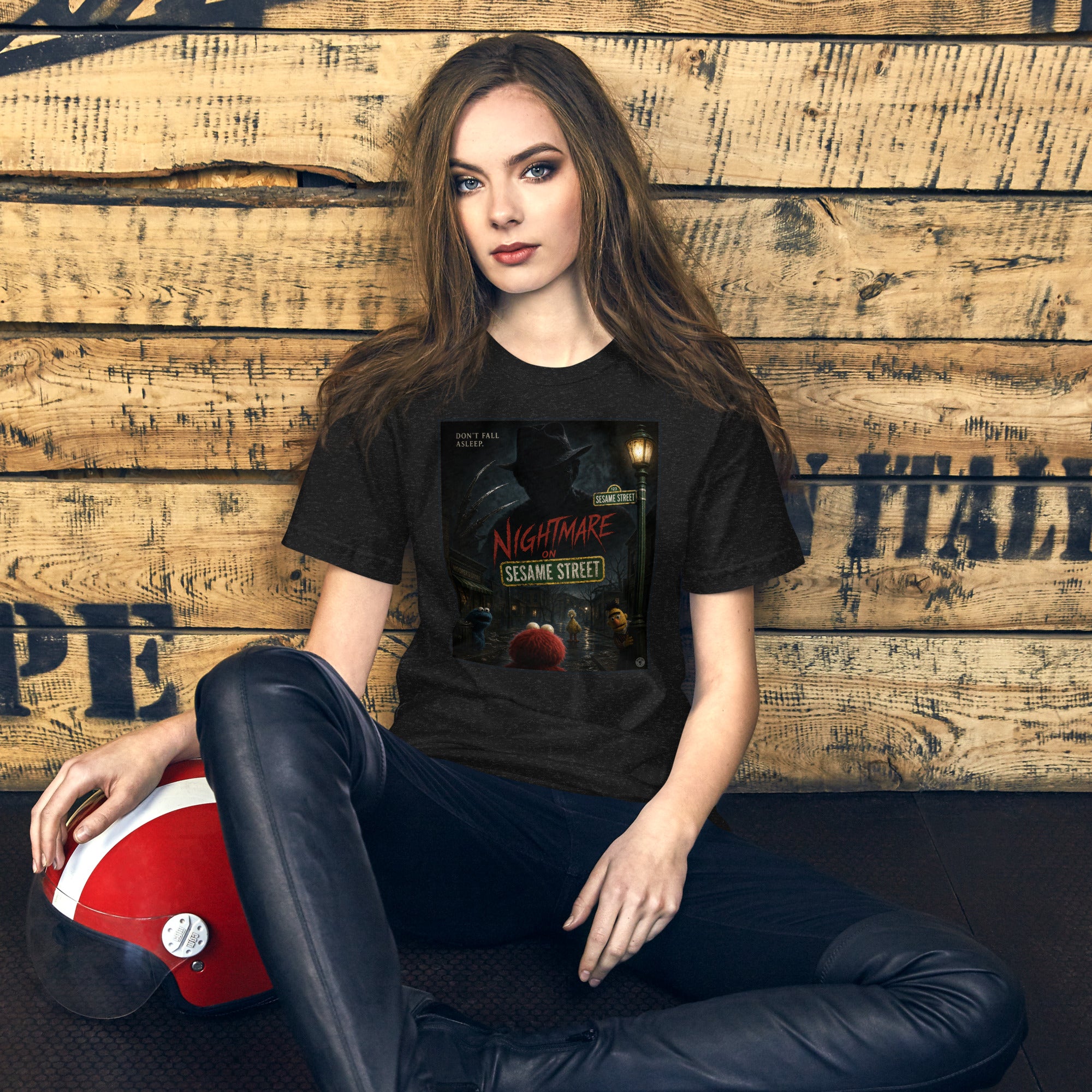 Person wearing a black t-shirt with 'Nightmare on Sesame Street' graphic, sitting against a wooden wall.