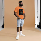 Man wearing an orange t-shirt with a graphic design, light blue shorts, and white sneakers in a studio setting.