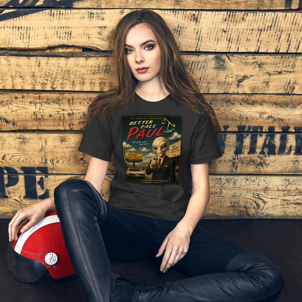 Woman wearing a black t-shirt with a graphic design, sitting against a wooden wall.