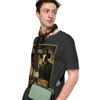 Man wearing a black t-shirt with a graphic design of a cow in a hat and scarf, holding a green bag.