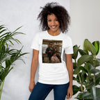 Person wearing a white t-shirt with a funny cool  graphic design, standing between two plants against a light background