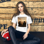 Woman wearing a white t-shirt with a graphic design, sitting against a wooden wall.