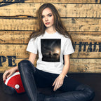Woman wearing a white t-shirt with a graphic design, sitting against a wooden wall.
