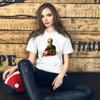 A woman sits cross-legged against a rustic wooden wall, wearing a white graphic T-shirt with a alien character and the text 'Better Call Paul' in red and yellow, paired with black pants. A red and white helmet rests beside her.