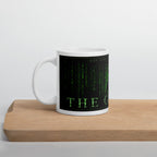 White mug with green text on a black background, placed on a wooden surface with a light gray background