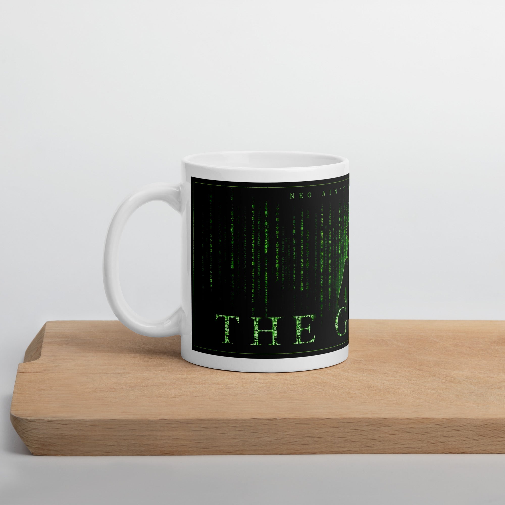 White mug with green text on a black background, placed on a wooden surface with a light gray background