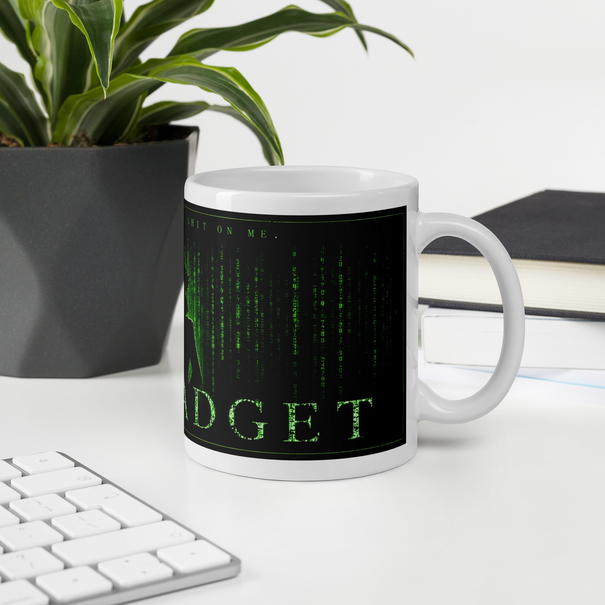 Mug with Matrix-themed design on a desk with keyboard, plant, and notebook.