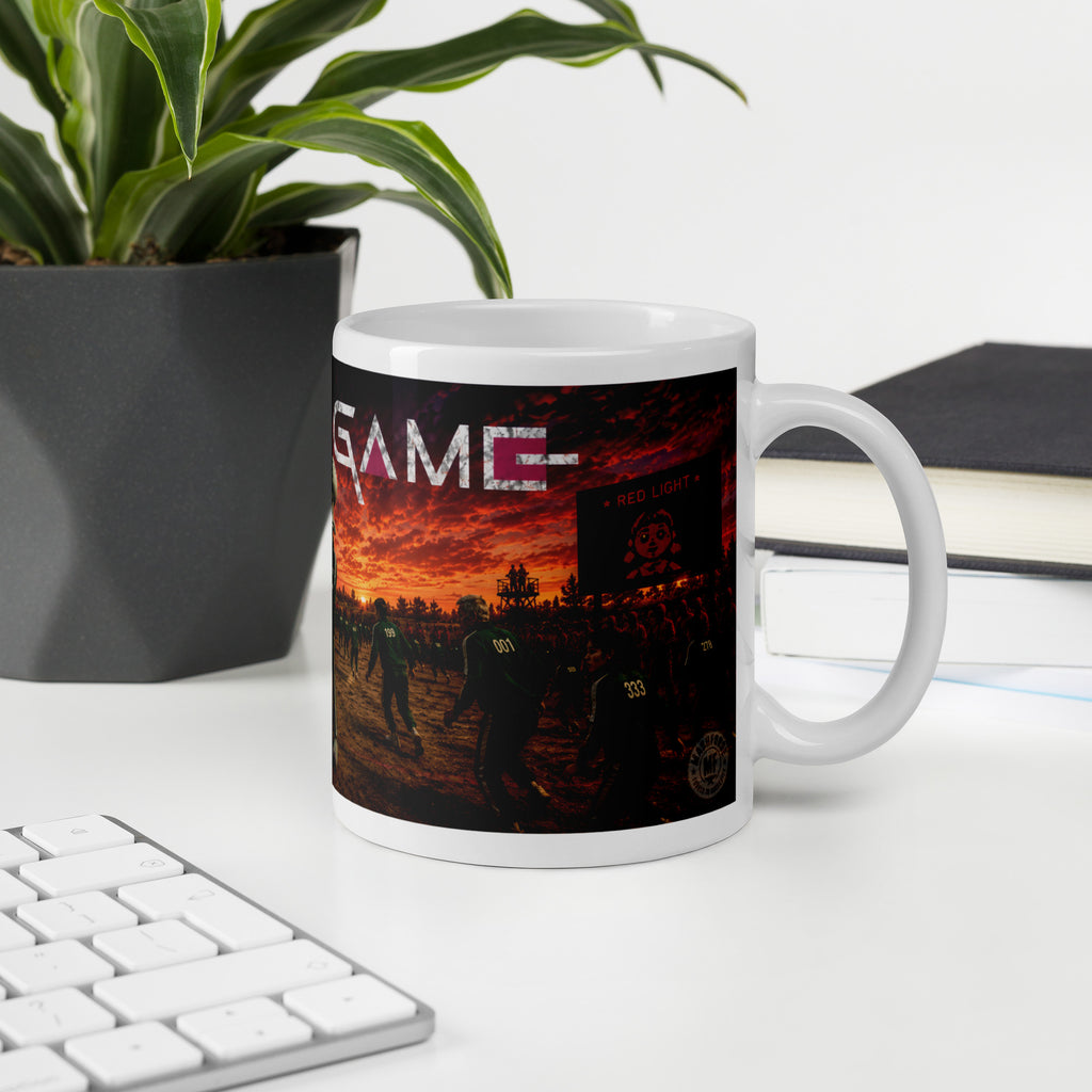 Mug with a sunset design and 'squid  GAME' text on a desk with a plant and books.