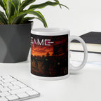 Mug with a sunset design and 'squid  GAME' text on a desk with a plant and books.